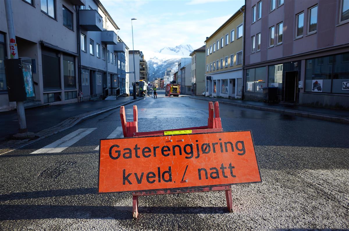 Gateskilt med skriften Gaterengjøring kveld/natt. Bildet er tatt under spyling av Gate 2 en dag i mai. I bakgrunnen ser man brannvesenet spyle, mens skiltet står i forgrunnen. - Klikk for stort bilde